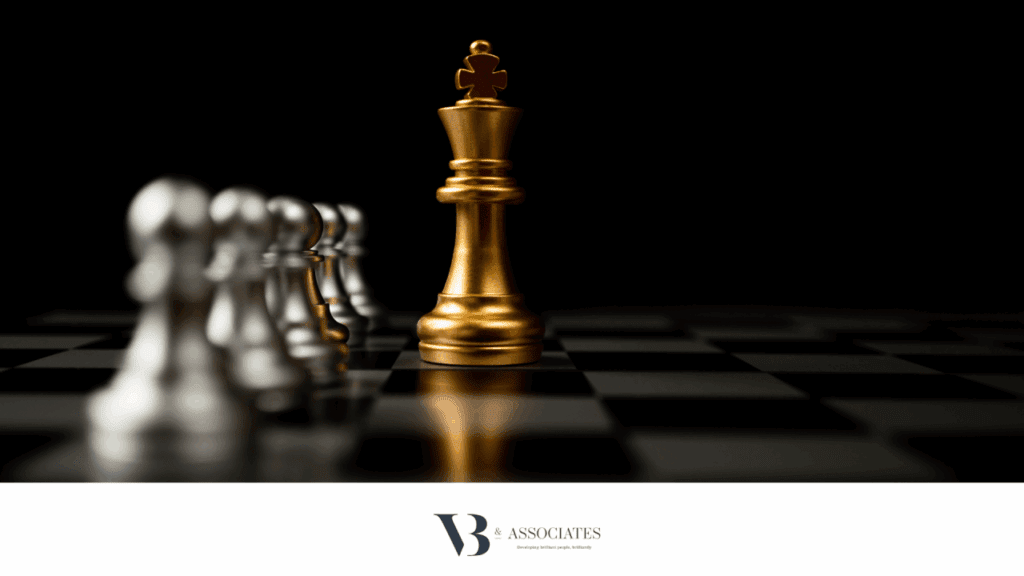 black background of a chess board, focusing on a large gold 'king' with silver other pieces to the side.