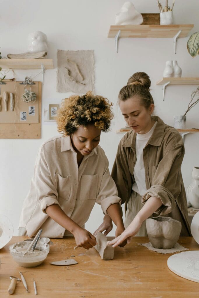 image of two women working together in a pottery workshop, with one woman showing the other how to do the task